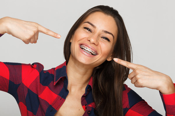 Woman with braces smiling and pointing at her mouth