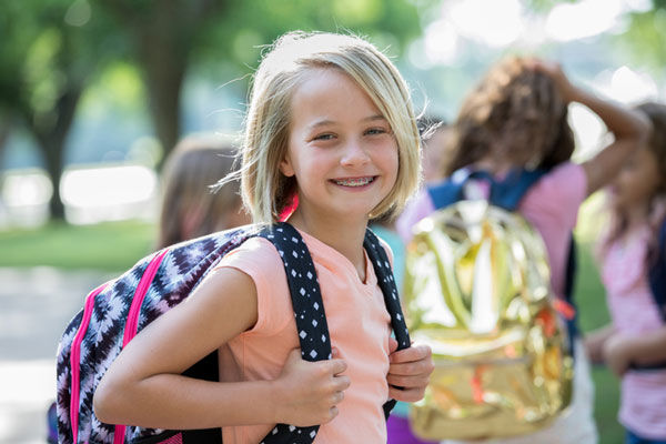 Young blonde girl carrying backpack and smiling with braces