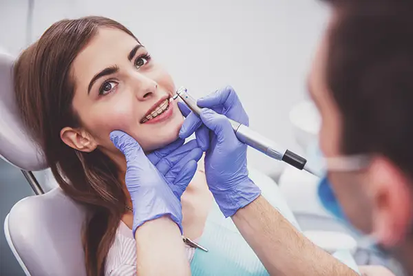 Dentist adjusting a young woman's braces during an orthodontic appointment, ensuring proper alignment.