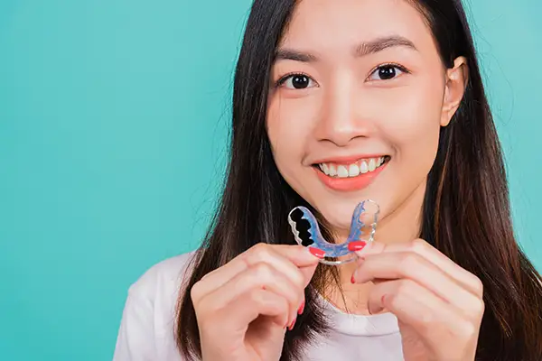 Happy young woman holding a colorful orthodontic retainer, emphasizing post-treatment care.