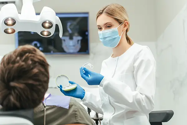 An orthodontist sits with a patient to review orthodontic treatment options, such as the clear aligners she holds in one hand, during a consultation appointment.