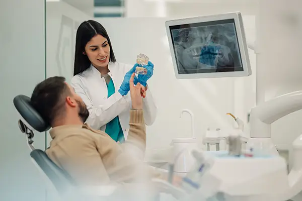 During a consultation appointment, a patient asks his orthodontist questions while she uses a dental model to explain the orthodontic issues he's experiencing.
