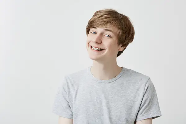 A teenage boy smiling and showing his teeth with traditional metal braces.
